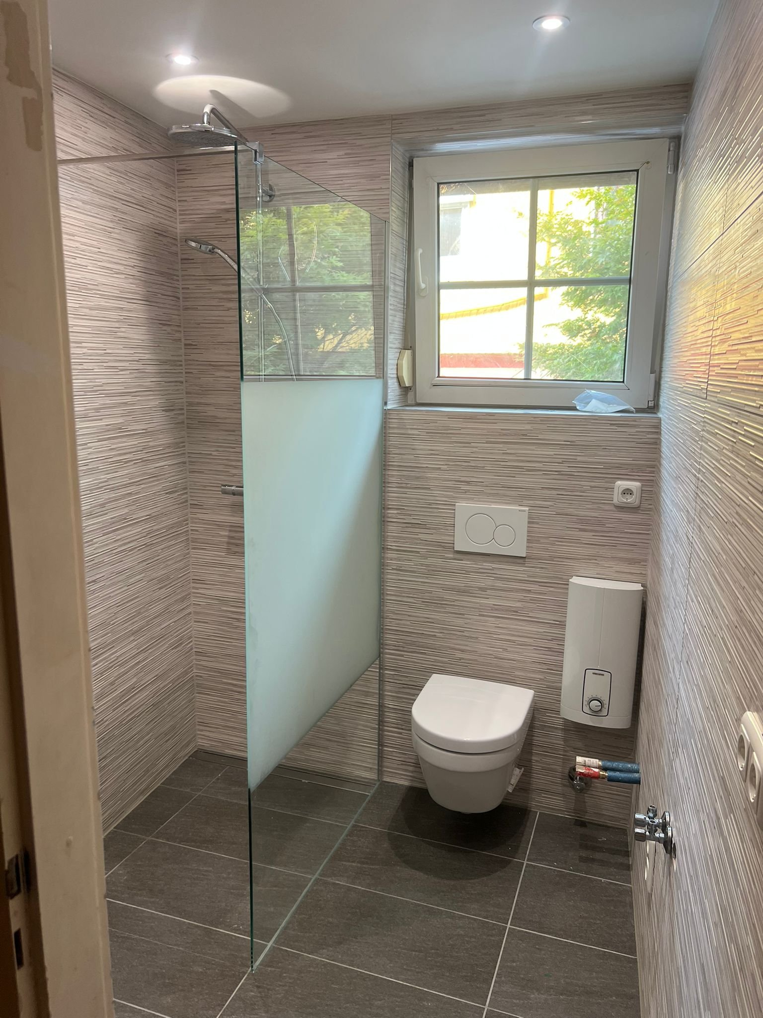 Fertig saniertes Bad mit bodengleicher Dusche, Glastrennwand, Fenster und wandhängendem WC