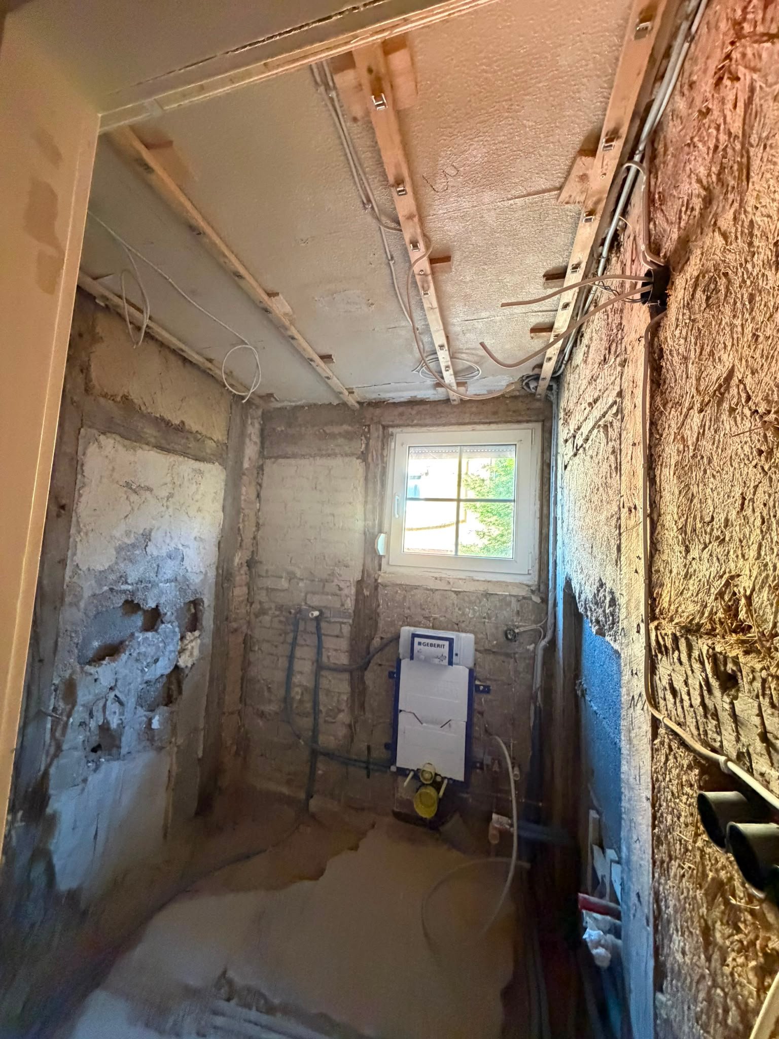 Entkerntes Bad vor der Sanierung: Vorwandelement für das WC, offene Leitungen, rohe Wände, Fenster in der Rückwand