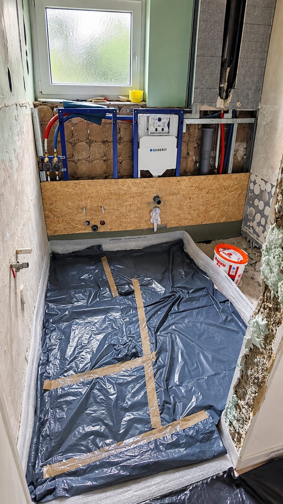 Bad während des Umbaus: Vorwandelemente für WC und Bidet, offene Wasserleitungen, der Boden mit Folie abgedeckt, Fenster in der Rückwand